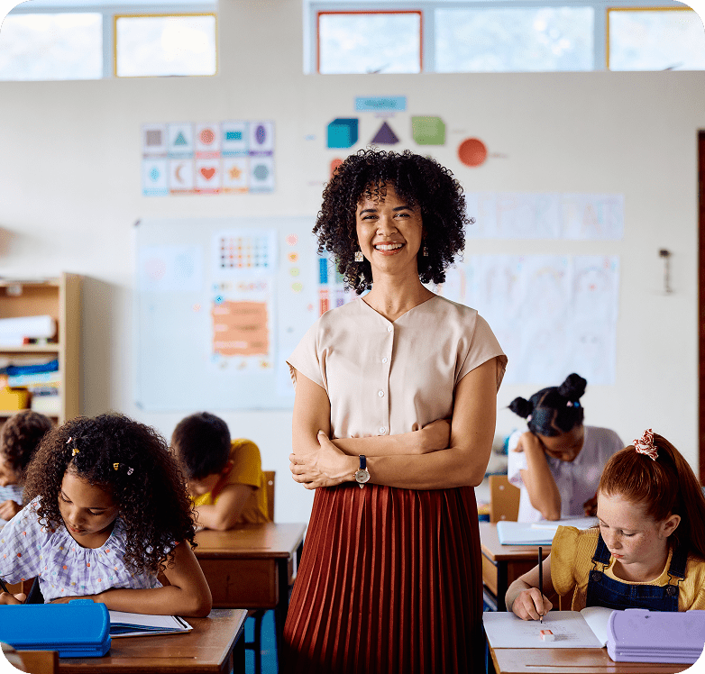 Teacher smiling in classroom with students writing.